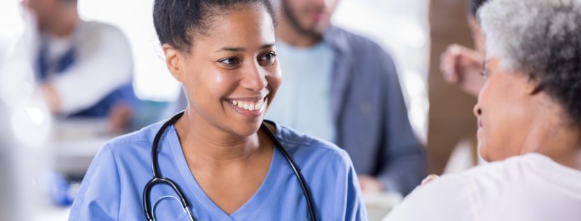 Smiling mid adult African American nurse talks with a senior woman. The nurse is volunteering in a free clinic.